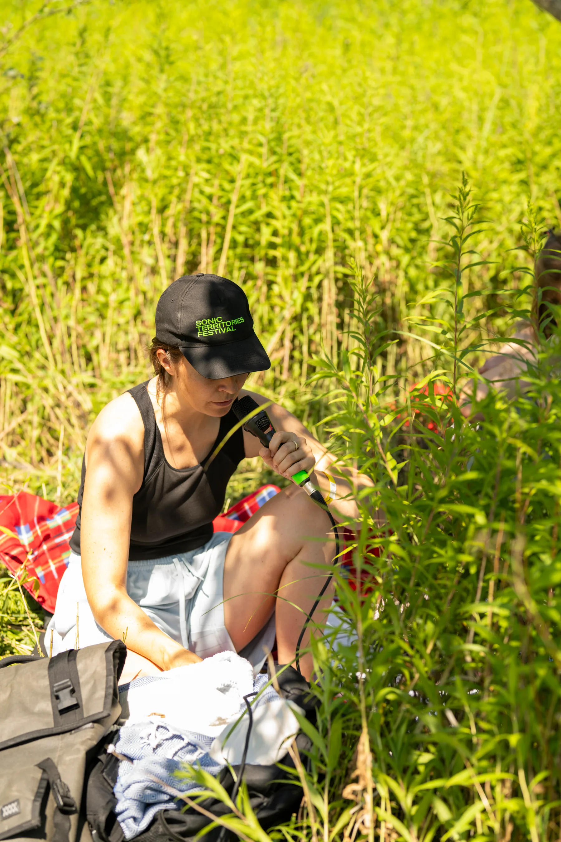 A participant seated in tall grass holds a microphone during Less is Sound